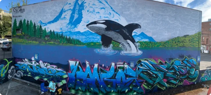Mural of an orca breaching in front of a mountain above graffiti lettering